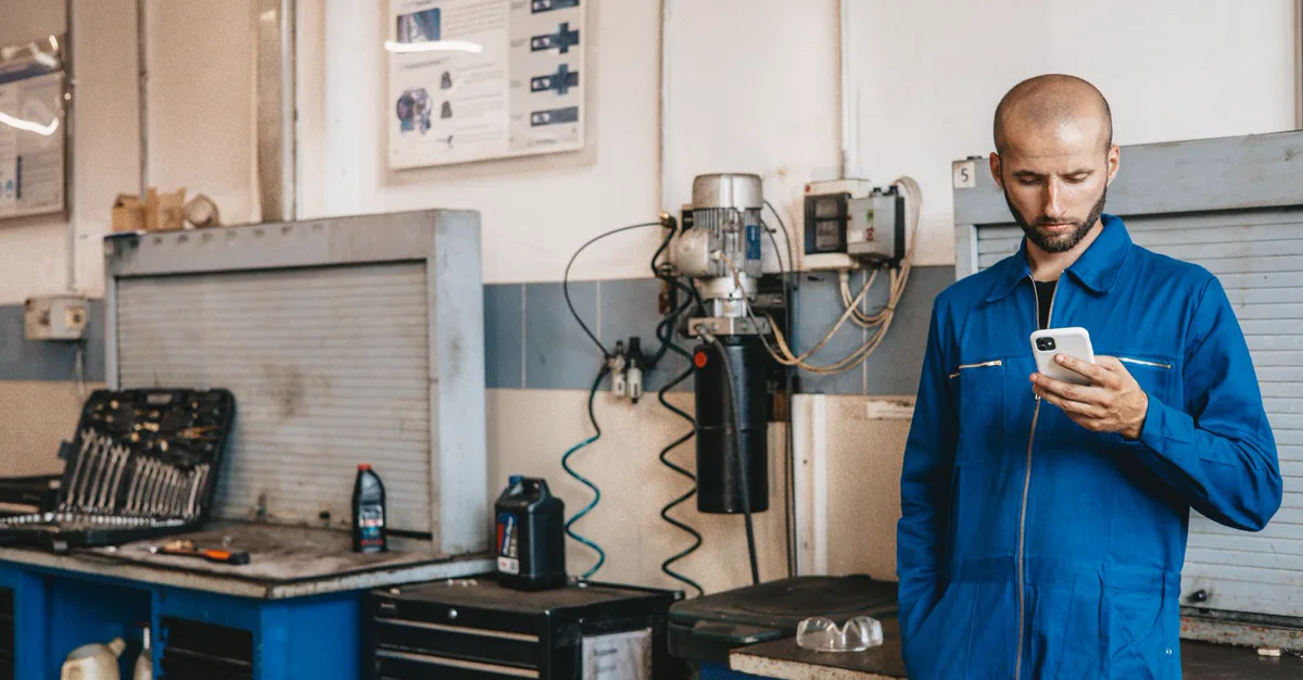 A mechanic in coveralls checking a smartphone in a repair workshop, the way most customers view a small business website.