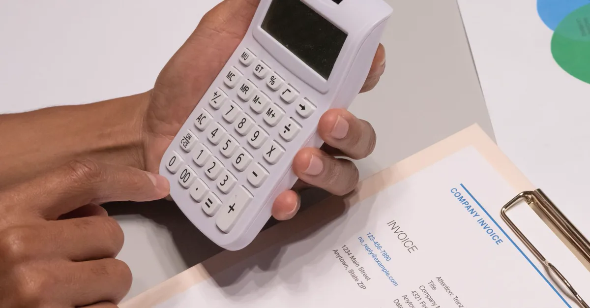 Hands using a calculator beside an invoice, working out the real cost of a monthly website plan.