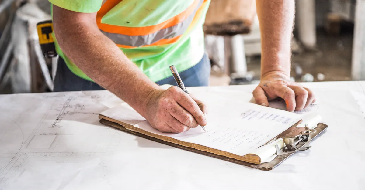 A contractor writing notes on a clipboard at a work site, planning contractor marketing ideas.