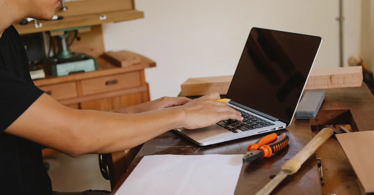 A tradesperson sitting at a table with their tools, working on a laptop.
