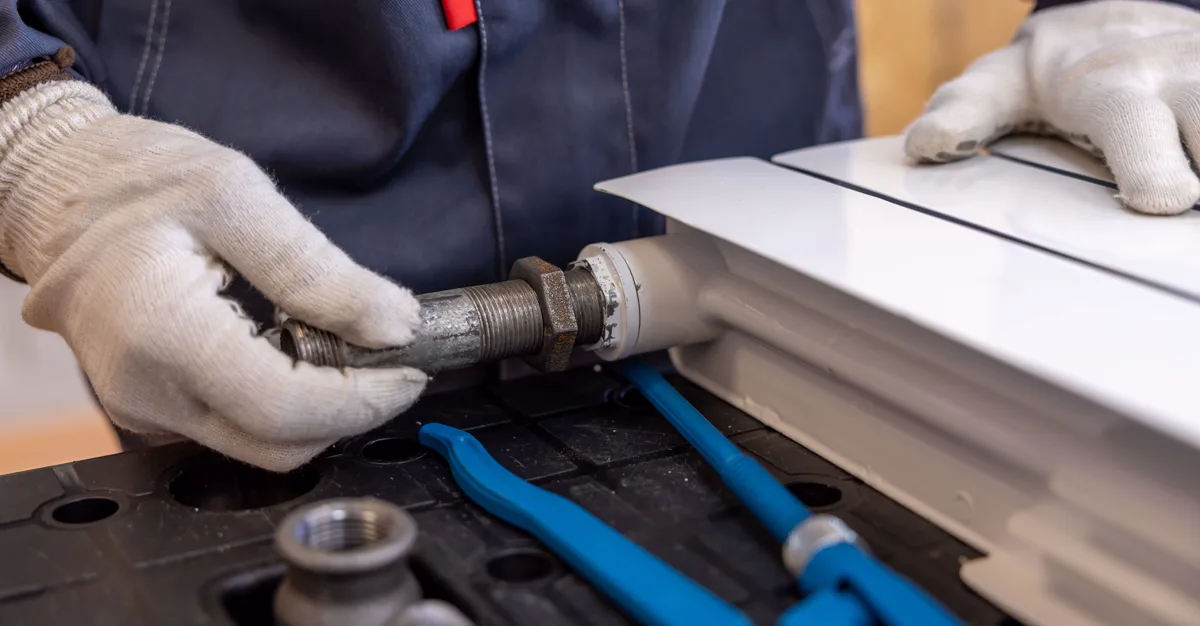 A plumber fitting a radiator pipe with a wrench, the kind of planned job that pricing pages win.