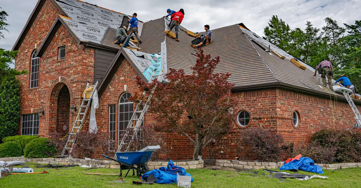 Roofers working on the roof of a brick home, replacing damaged shingles.