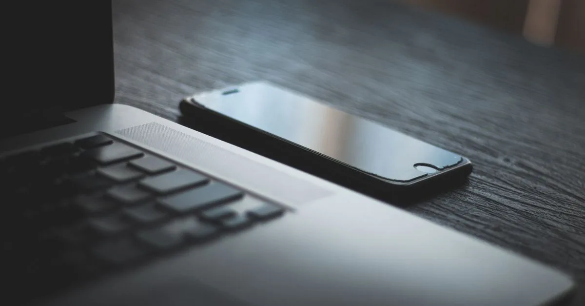 A smartphone and laptop on a desk, showing a contractor checking their website on mobile.