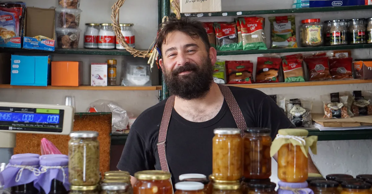 A small business owner standing behind shelves of homemade preserves in their shop.
